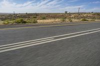 a motorcycle rider riding on an empty road in front of a mountain range with some grass and bushes