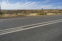 a motorcycle rider riding on an empty road in front of a mountain range with some grass and bushes