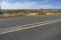 a motorcycle rider riding on an empty road in front of a mountain range with some grass and bushes