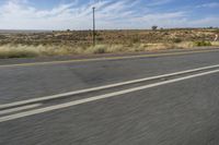 a motorcycle rider riding on an empty road in front of a mountain range with some grass and bushes