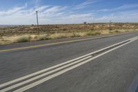 a motorcycle rider riding on an empty road in front of a mountain range with some grass and bushes