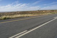 a motorcycle rider riding on an empty road in front of a mountain range with some grass and bushes