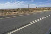 a motorcycle rider riding on an empty road in front of a mountain range with some grass and bushes