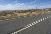a motorcycle rider riding on an empty road in front of a mountain range with some grass and bushes