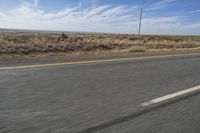 a motorcycle rider riding on an empty road in front of a mountain range with some grass and bushes