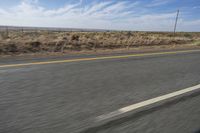 a motorcycle rider riding on an empty road in front of a mountain range with some grass and bushes