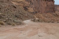 motorcycle rider jumping a hill on dirt road with rocks in background under cliff wall by roadway