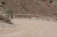 motorcycle rider jumping a hill on dirt road with rocks in background under cliff wall by roadway