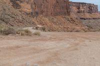 motorcycle rider jumping a hill on dirt road with rocks in background under cliff wall by roadway