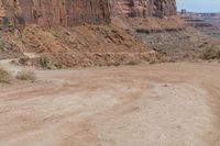 motorcycle rider jumping a hill on dirt road with rocks in background under cliff wall by roadway