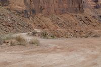 motorcycle rider jumping a hill on dirt road with rocks in background under cliff wall by roadway