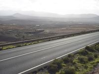 the motorcycle rider rides a long stretch of road with a mountainous background and mountains around it