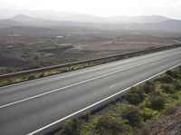 the motorcycle rider rides a long stretch of road with a mountainous background and mountains around it
