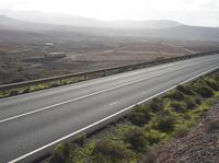 the motorcycle rider rides a long stretch of road with a mountainous background and mountains around it