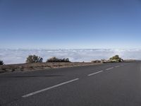 a motorcycle rider riding on an asphalt highway in the mountains and over rolling clouds with blue sky behind him