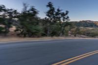 a motorcycle rider taking a sharp turn on an empty road during sunset hours, with trees surrounding