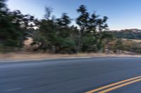 a motorcycle rider taking a sharp turn on an empty road during sunset hours, with trees surrounding