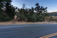 a motorcycle rider taking a sharp turn on an empty road during sunset hours, with trees surrounding