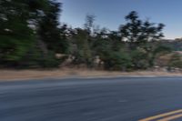 a motorcycle rider taking a sharp turn on an empty road during sunset hours, with trees surrounding