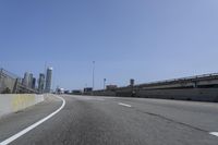 a person riding a motorcycle along a road next to a bridge with buildings behind them