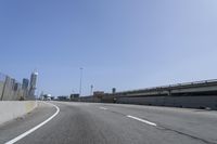 a person riding a motorcycle along a road next to a bridge with buildings behind them