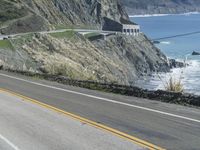 a motorcycle is riding down the coastal highway on a sunny day while a person on a bike stands at the corner