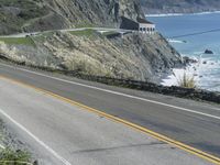 a motorcycle is riding down the coastal highway on a sunny day while a person on a bike stands at the corner