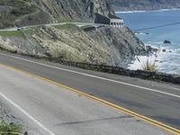 a motorcycle is riding down the coastal highway on a sunny day while a person on a bike stands at the corner