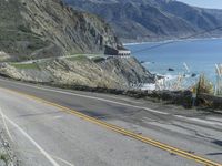 a motorcycle is riding down the coastal highway on a sunny day while a person on a bike stands at the corner