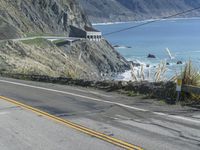 a motorcycle is riding down the coastal highway on a sunny day while a person on a bike stands at the corner