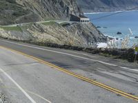 a motorcycle is riding down the coastal highway on a sunny day while a person on a bike stands at the corner