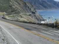 a motorcycle is riding down the coastal highway on a sunny day while a person on a bike stands at the corner