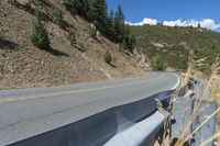 a motorcycle riding up the side of a road next to a grassy hillside under blue skies