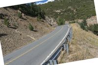 a motorcycle riding up the side of a road next to a grassy hillside under blue skies