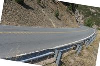 a motorcycle riding up the side of a road next to a grassy hillside under blue skies