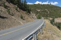 a motorcycle riding up the side of a road next to a grassy hillside under blue skies