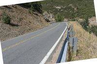 a motorcycle riding up the side of a road next to a grassy hillside under blue skies