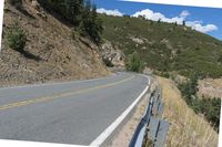 a motorcycle riding up the side of a road next to a grassy hillside under blue skies