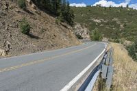 a motorcycle riding up the side of a road next to a grassy hillside under blue skies