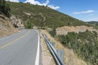 a motorcycle riding up the side of a road next to a grassy hillside under blue skies