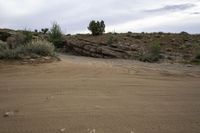 a motorcycle is driving on a dirt road in the desert with rocks and scrub on it