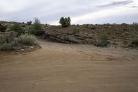 a motorcycle is driving on a dirt road in the desert with rocks and scrub on it