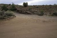 a motorcycle is driving on a dirt road in the desert with rocks and scrub on it