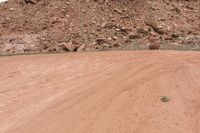 a person rides a yellow motorcycle down a dirt road next to a mountain of rocks