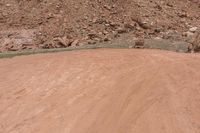 a person rides a yellow motorcycle down a dirt road next to a mountain of rocks