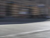 a person riding a motorcycle down the street in motion, with blurry buildings and trees in the background