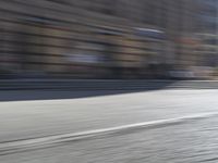 a person riding a motorcycle down the street in motion, with blurry buildings and trees in the background