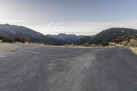 a motorcycle is going down an empty road by the mountains and trees at sunset time