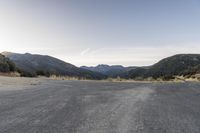 a motorcycle is going down an empty road by the mountains and trees at sunset time