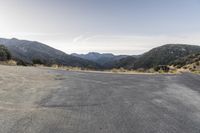 a motorcycle is going down an empty road by the mountains and trees at sunset time